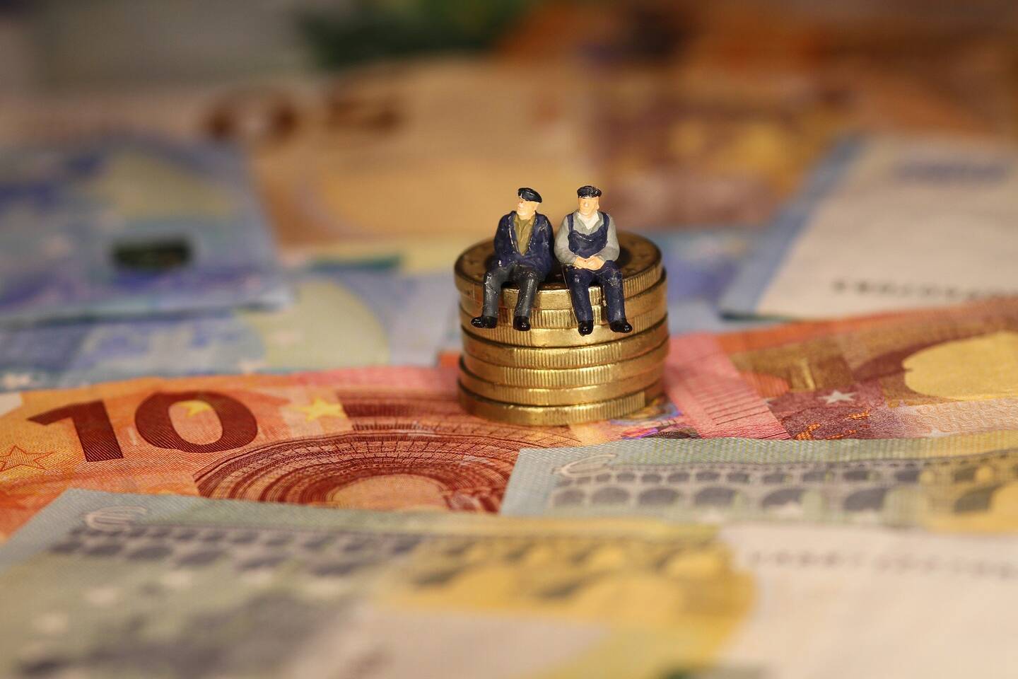 twee figuurtjes op een stapel euro munten met daaronder briefgeld in euros