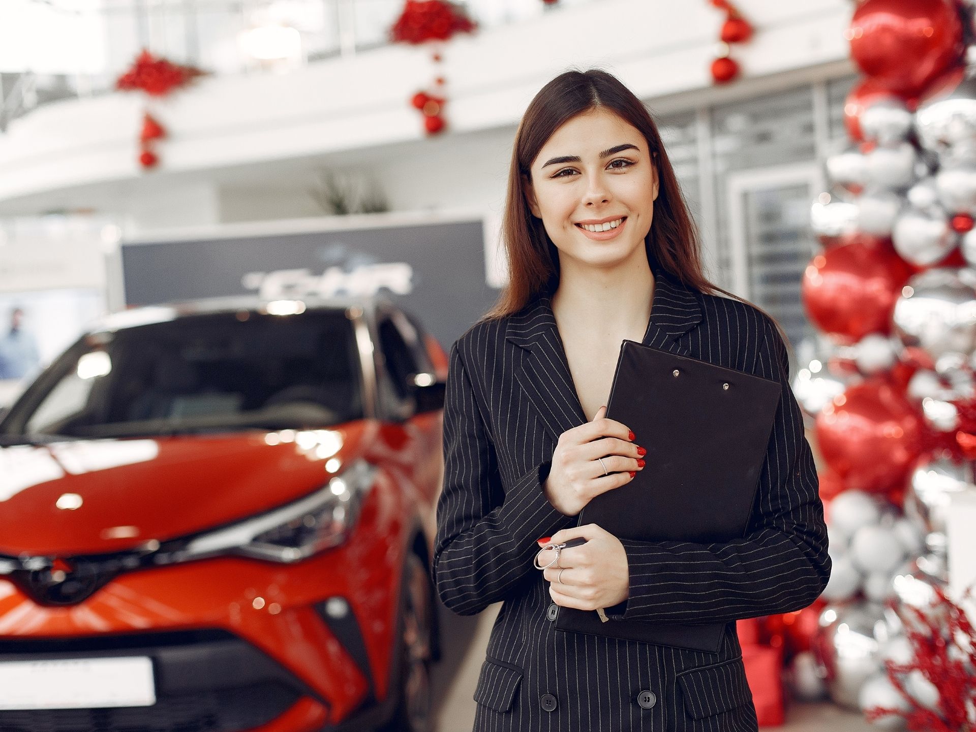 Vrouw van lease'm bij rode auto in een versierde showroom